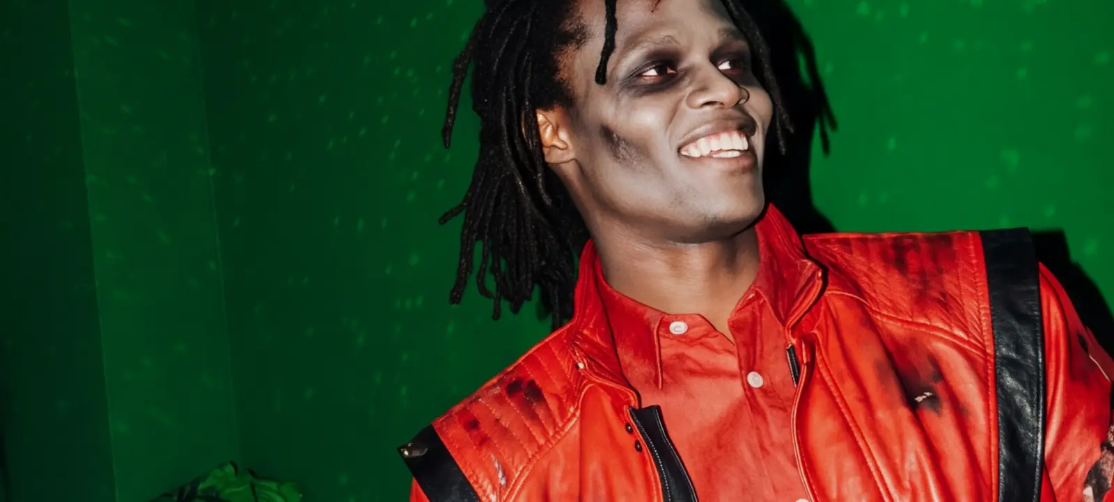 Guest in a red 80s leather jacket with zombie make-up in front of a green wall