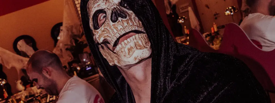 Guest in a skull mask and black hooded cloak at the bar